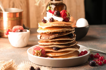 tasty american pancakes in stack with sour cream and fresh berries on white plate on table near wooden background