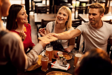Group of happy friends paying restaurant check to a waiter.