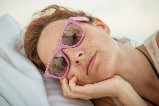 Beautiful female in trendy shades looking at camera while lying on soft bean bag on sunny day in Maldives