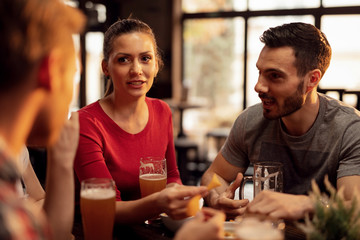 Group of friends talking while drinking beer and eating nacho chips in a pub.
