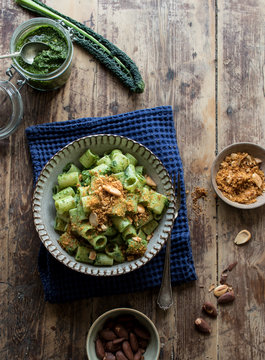 From above bowl of palatable pasta paccheri with fresh kale pesto and ground peanuts on timber tabletop