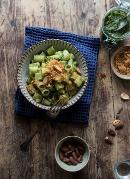 From above bowl of palatable pasta paccheri with fresh kale pesto and ground peanuts on timber tabletop