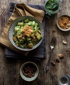 From above bowl of palatable pasta paccheri with fresh kale pesto and ground peanuts on timber tabletop