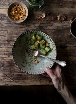 From above crop hands taking bowl of delicious pasta paccheri with tasty kale pesto and ground peanuts over wooden tabletop
