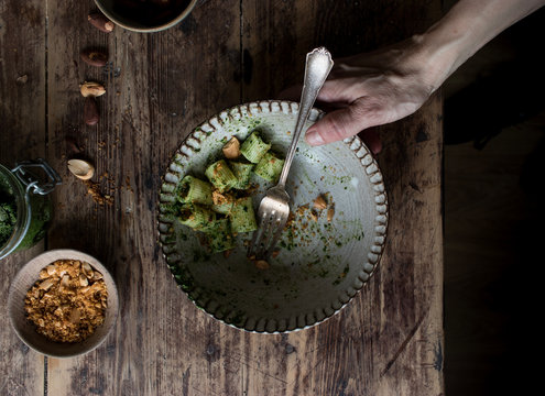 From above crop hands taking bowl of delicious pasta paccheri with tasty kale pesto and ground peanuts over wooden tabletop