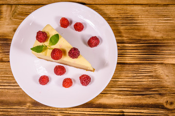 White plate with cheesecake New York, leaf of mint and raspberries on wooden table. Top view