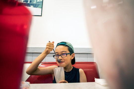A young boy eating a milkshake for desert inside a restaurant.