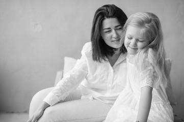 Mother and daughter indoor lifestyle black white portrait. Mom with child have fun in studio. Happiness of motherhood. Mother hugs with her little daughter. Young emotional girl  embraces her mom.