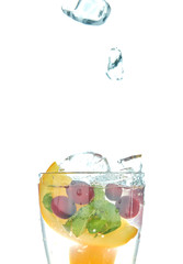 orange splashing into a glass of water with mint and berries on a white background. refreshing summer drink with citrus.