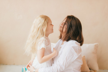 Mother and daughter indoor lifestyle portrait. Mom with child have fun in studio on yellow wall. Happiness of motherhood. Mother hugs with her little daughter. Young emotional girl  embraces her mom.