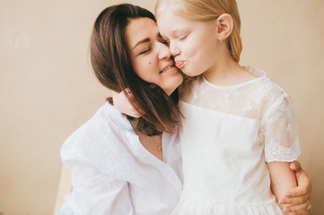 Mother and daughter indoor lifestyle portrait. Mom with child have fun in studio on yellow wall. Happiness of motherhood. Mother hugs with her little daughter. Young emotional girl  embraces her mom.