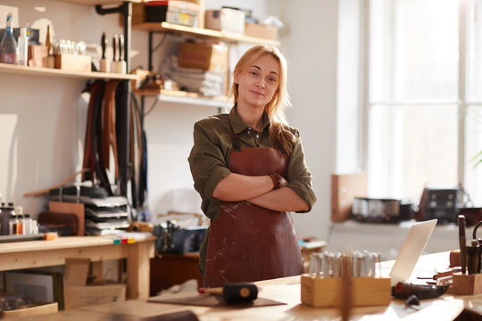 Warm toned portrait of confident female artisan standing with arms crossed while posing in workshop