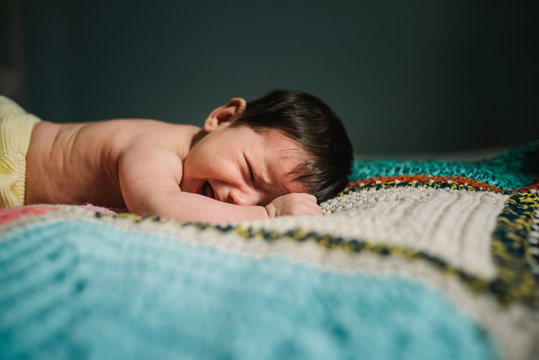 Cute shirtless baby lying on warm knitted blanket and crying loudly in cozy nursery