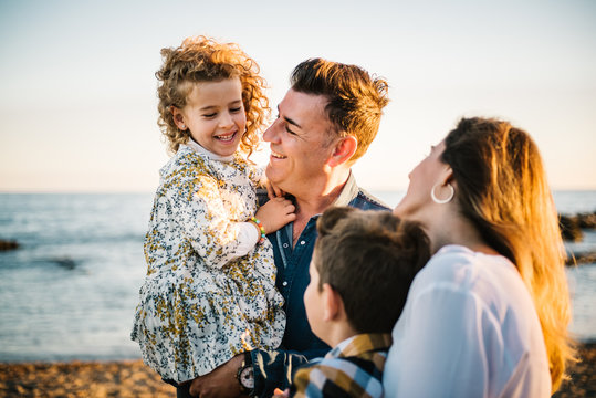 Middle aged man an woman with children at sea shore smiling and hugging each other