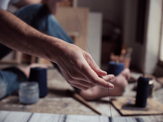 Unrecognizable male artist preparing thin dark thread while creating abstract painting on floor of workshop