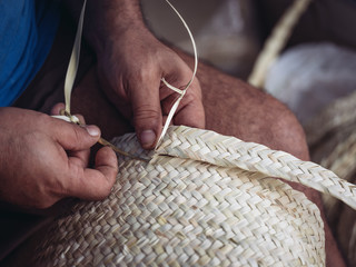 Hands of anonymous artisan showing lovely basket with floral ornament braided from dried palm fiber
