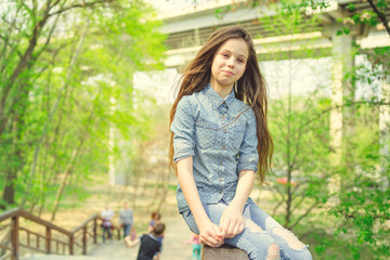 Glad girl sitting on railing Pleased girl in casual outfit looking at camera while sitting on wooden railing of stairway in green park