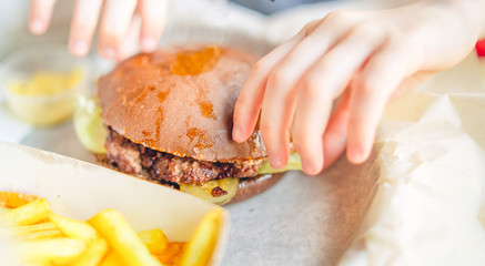 Hamburger and french fries on table in cafe. Hot tasty hamburger with meat and vegetables like lettuce and onion and french fries on table in restaurant