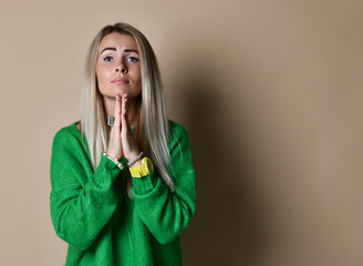 Indoor shot of regretful woman looks gloomy and desperate, keeps palms together, beggs for...