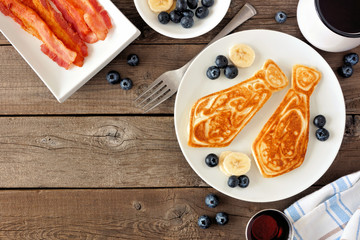 Tie shaped pancakes with blueberries and bananas. Fathers Day brunch concept. Top view corner border on a rustic wood background.