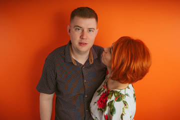 Couple of lovers on an orange background. The husband and wife, the concept of family. Young man and woman with bright red hair