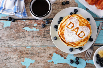 Pancakes with heart shape and DAD letters. Fathers Day breakfast concept. Above view corner border on a blue wood background.