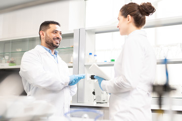 Cheerful positive young multi-ethnic laboratory colleagues in white coats standing in modern...