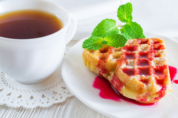 Homemade waffle and a cup of tea on a white wooden table.