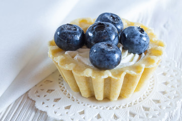 Tartlet or cake with fresh blueberries and cream cheese on white wooden background.