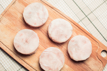 Chunks of frozen fish fillet hake on wooden cutting board.