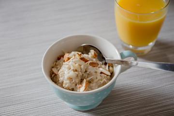 Bowl of homemade oatmeal porridge with almonds and orange juice