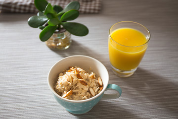 Bowl of homemade oatmeal porridge with almonds and orange juice