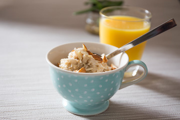 Bowl of homemade oatmeal porridge with almonds and orange juice