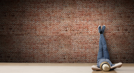 Obraz premium Young man lying on the floor with legs raised up on the wall. Mixed media