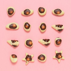 Chocolates in the form of sea shellfish and shells on a light pink background. Flat lay.