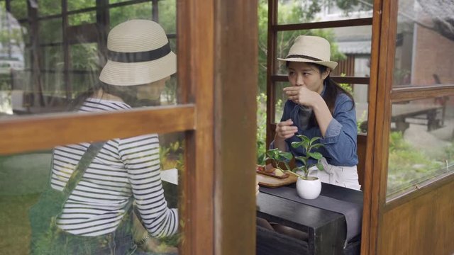 two smiling asian women friends travel in kyoto japan experience japanese culture chodo ceremony. young girls tourists chatting drinking tea laughing wearing straw hat sit at wooden table by teien