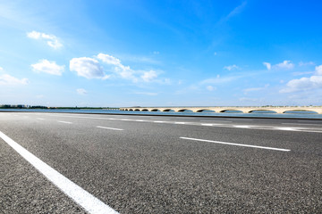Empty asphalt road and lake with bridge under blue sky