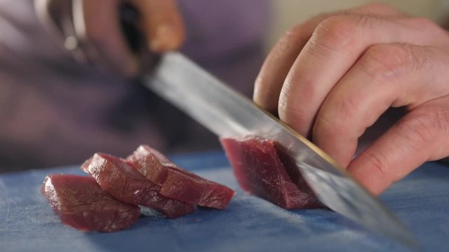 close up macro on the hands of the Japanese sushi sashimi chef 's knife, slice the raw tuna salmon fish for cooking maki sushi (Summer row) in the kitchen.