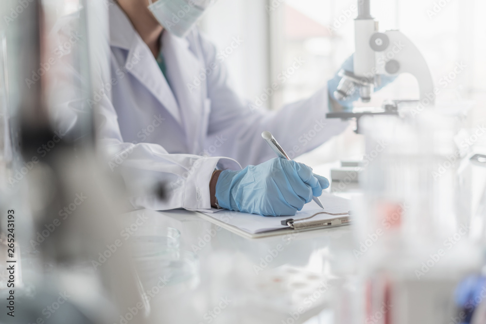 Wall mural a scientist hands writing on a clipboard in laboratory with test tube microscope and solutions.