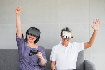 Old senior Asian couple enjoy playing vdo game wearing VR headset.