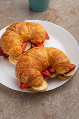 fresh croissant on the table, with hot tea, strawberries and bananas, delicious breakfast