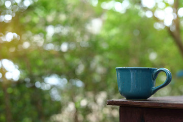 green mug of hot drink put on wooden table in nature of morning day