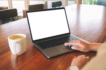 Fototapeta premium Mockup image of a woman's hand using and touching on laptop touchpad with blank white desktop screen with coffee cup on wooden table