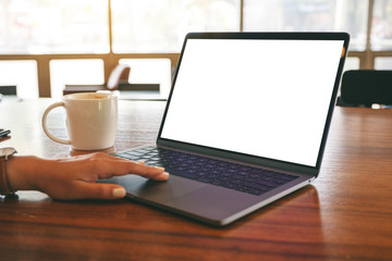 Fototapeta premium Mockup image of a woman's hand using and touching on laptop touchpad with blank white desktop screen with coffee cup on wooden table