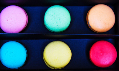 Tasty different colored macarons in black box on multicolored background