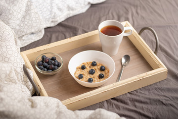 oatmeal with berries on a tray in bed with tea, morning breakfast and mood