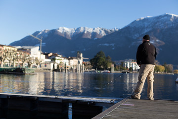 Ascona Lake Maggiore 2 December 2012: Man holds long fishing rod and fishes at lake surrounded by beautiful countryside