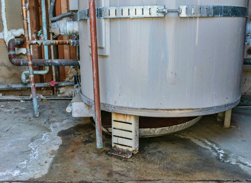 Water heater leaks from the bottom to the floor. Overflowing water heater drip pan. It is time to call a plumbing service for inspection, repair or replacement