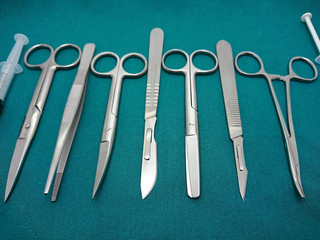 Stainless steel of surgical instrument, scalpel, tweezers, scissors, syringe on surgical green drape fabric.