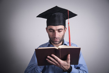 Man with graduation hat reading book. Education